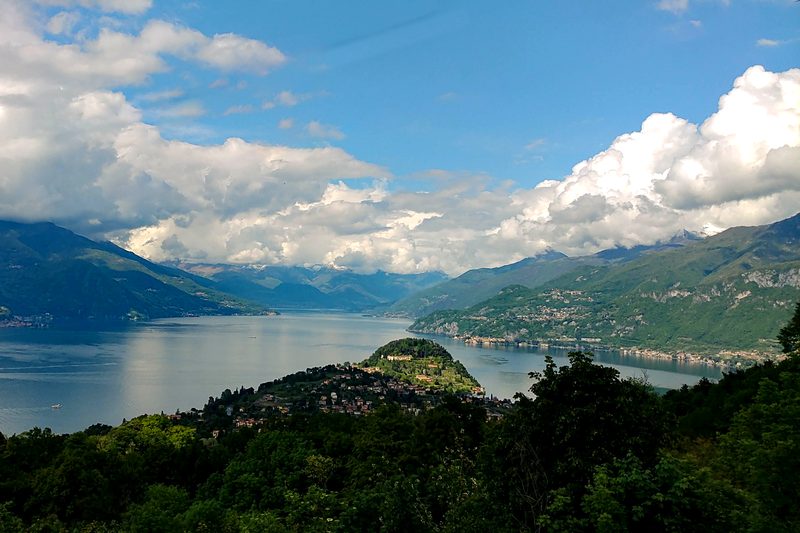 Lake Como seen from the hills above, with mountains, clouds and a wooded peninsula