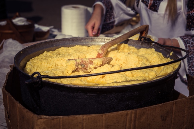 A large black pot of creamy golden polenta being stirred with a wooden spoon